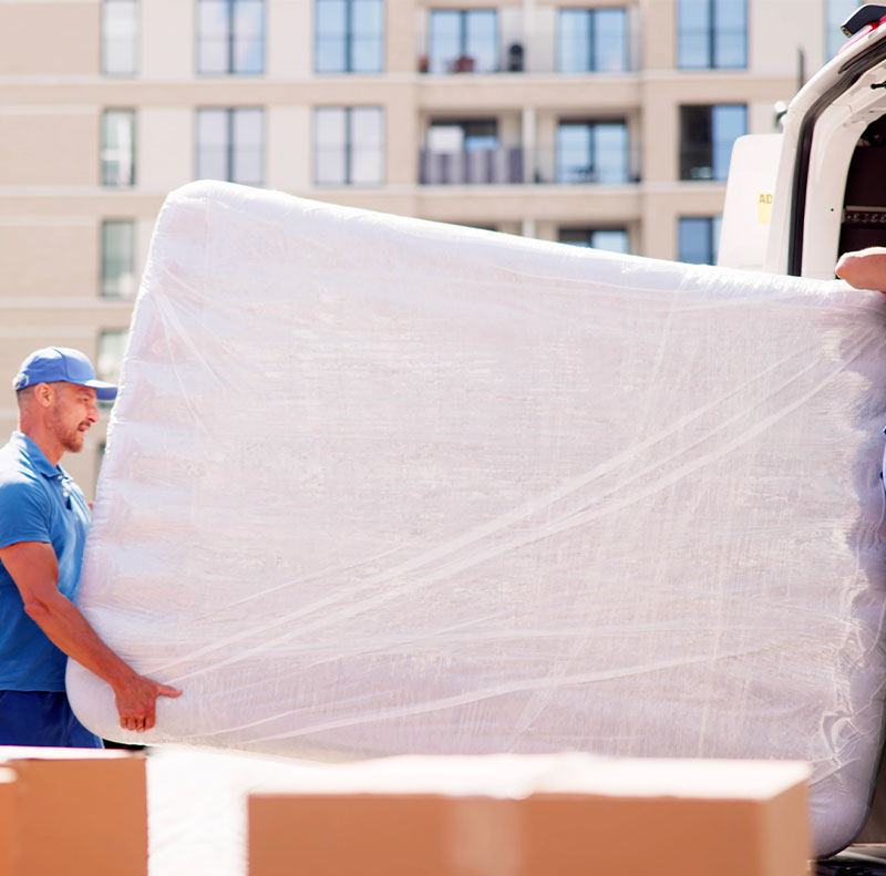 Due addetti ai traslochi trasportano un grande materasso da smaltire avvolto in plastica