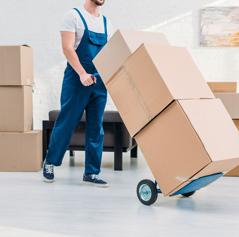 Un addetto ai traslochi in tuta da lavoro utilizza un carrello per spostare in modo efficiente una pila di grandi scatoloni di cartone